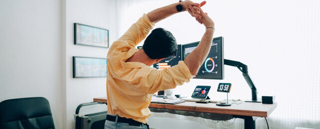 man stretching while standing at his desk