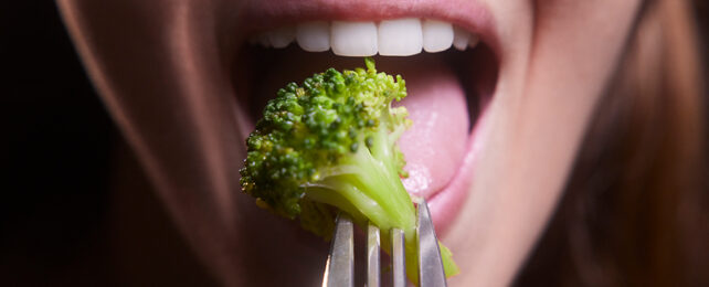 woman eating broccoli on a fork