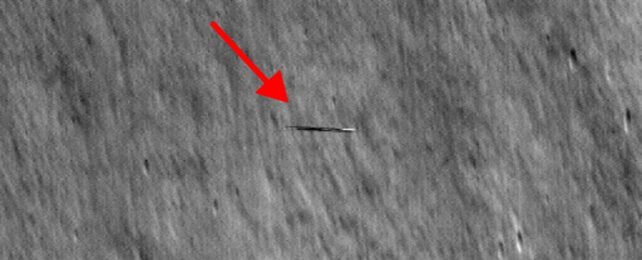 Grey scale photo of moon surface with a red arrow pointing at a small object in the center