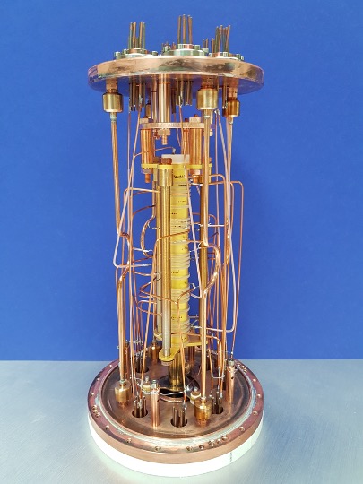 Cylindrical gold device used in particle physics experiment, photographed on a white table and blue background.