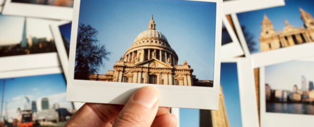 Close up of hand holding Polaroid image of a building, with other Polaroids scattered in the background.