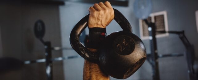 A close up of a hand gripping a kettlebell in a gym