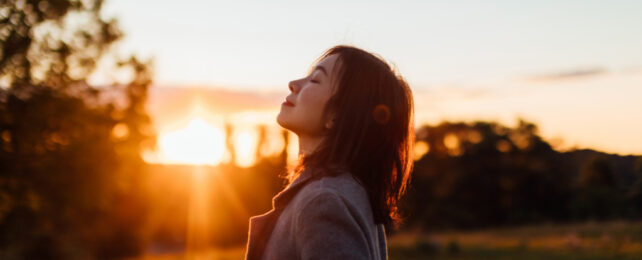 Asian woman inhaling fresh air outdoors as sun sets.