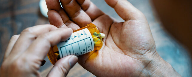 hand shaking out pills from an orange bottle