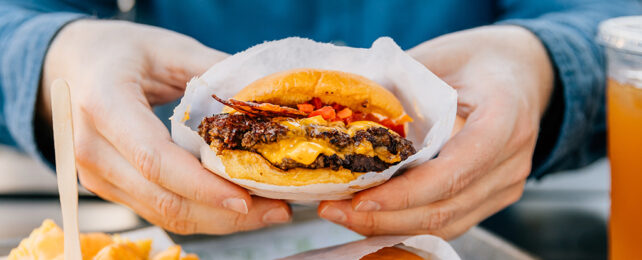 hands holding a cheeseburger in a bag