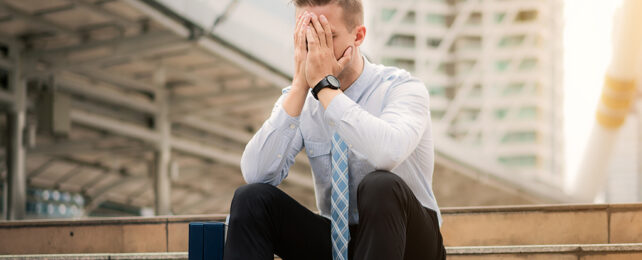 man holding face in hands sitting on steps