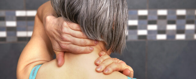 older woman rubbing back of her neck with hands