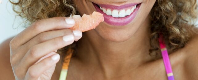 A smiling mouth and a hand holding a piece of fruit