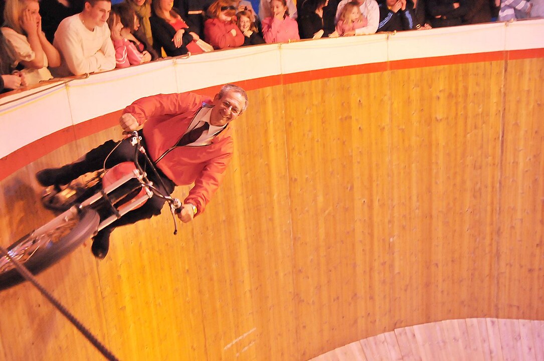 Man riding bike on wall of circular arena, basically horizontal