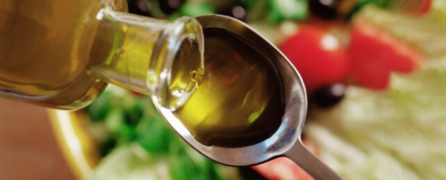 Olive oil being poured into a tablespoon in front of a salad