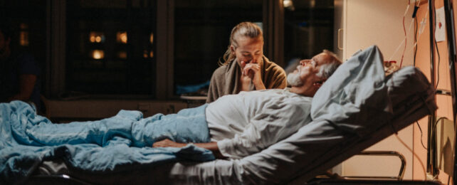 Women holding hand of hospital patient lying in bed.