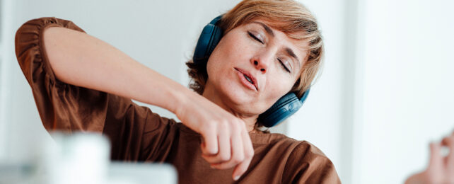 Woman with eyes closed and headphones on pretending to play a violin
