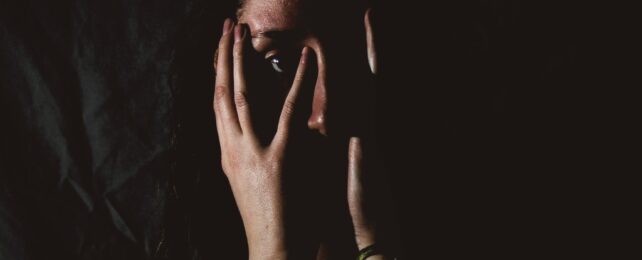 A face with hands covering it, shadowed with a dark background