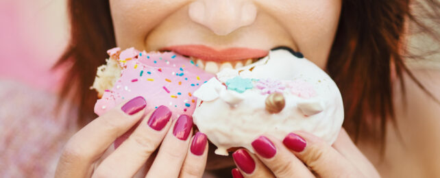 Lady pushing two brightly colored cupcakes into her mouth