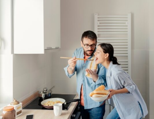 A young couple cooking dinner and tasting food on a spoon