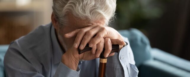Elderly man resting head on hands holding walking cane