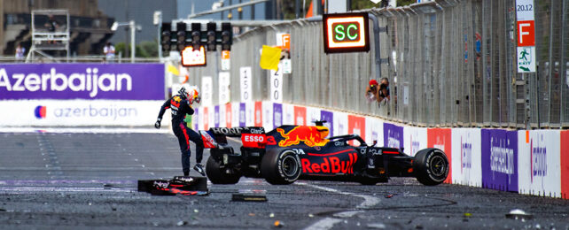 long shot of max verstappen standing on the formula 1 track with his black Redbull racing car crashed against the rail. he is kicking the car. a sign in the background says 'azerbaijan'. two photographers peek out from the rail cage behind verstappen, to take pictures of the crash.