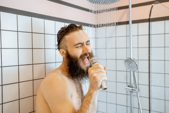 A man with a beard singing into a microphone while in the shower