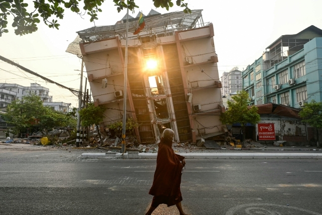 A monk walks past a collapsed building