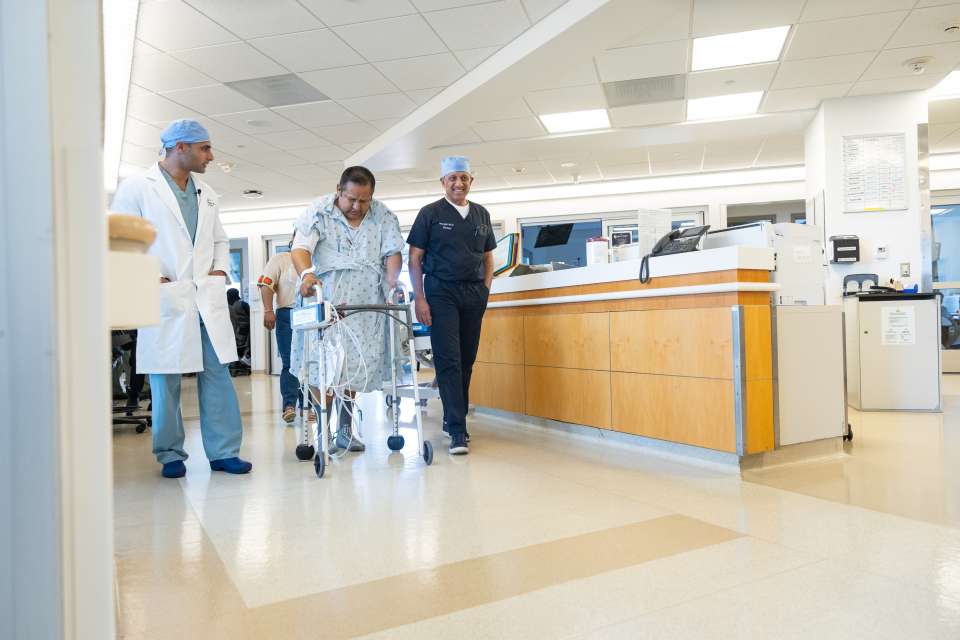 Two doctors flanking a patient with a walker in a hospital