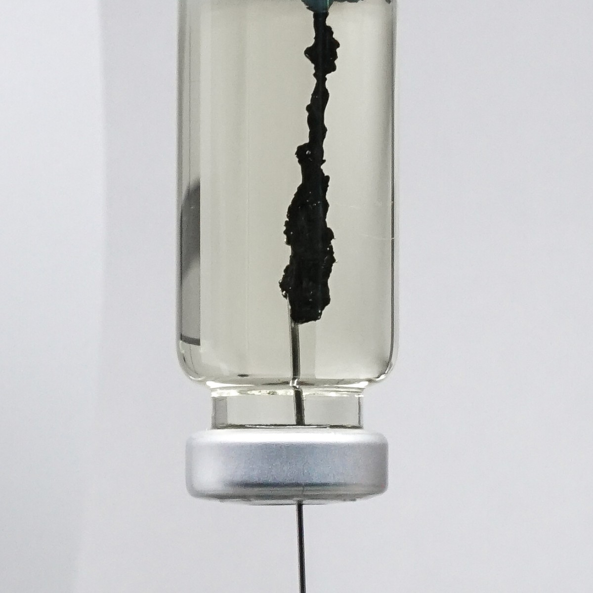 photo of a glass vial with a syringe extruding black material into a clear solution.
