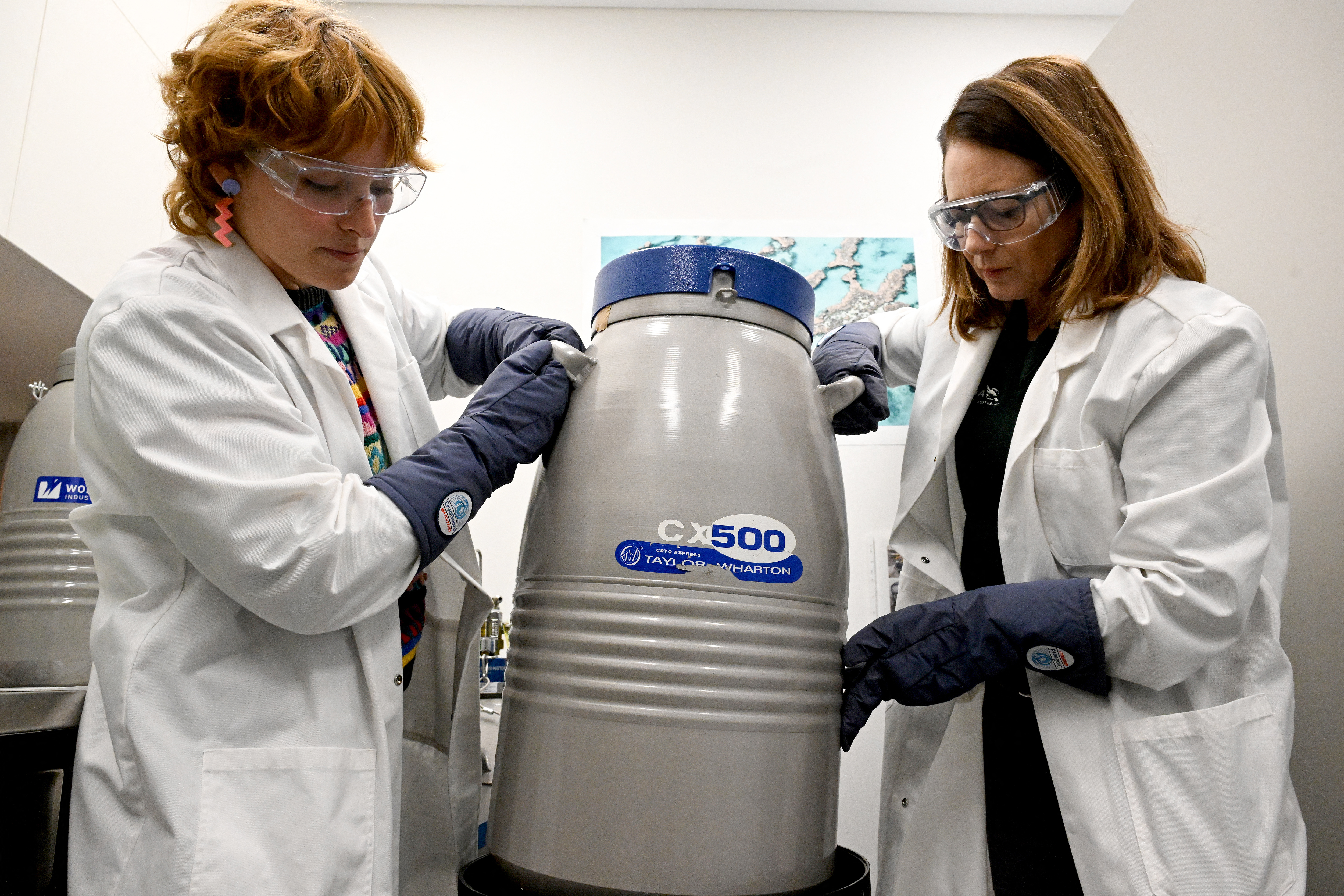 Two women in lab coats moving big cylindrical tank