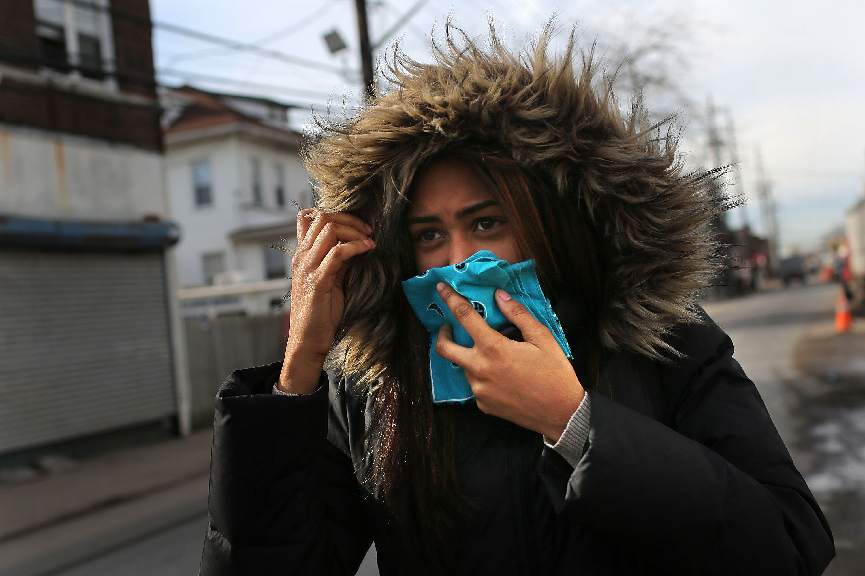 portrait of a woman wearing a fur hood holding a hanky to her face as she walks through a damaged new york queens neighbourhood