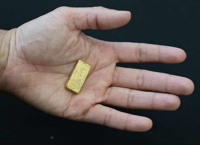 Person holding a small gold brick in the palm of their hand