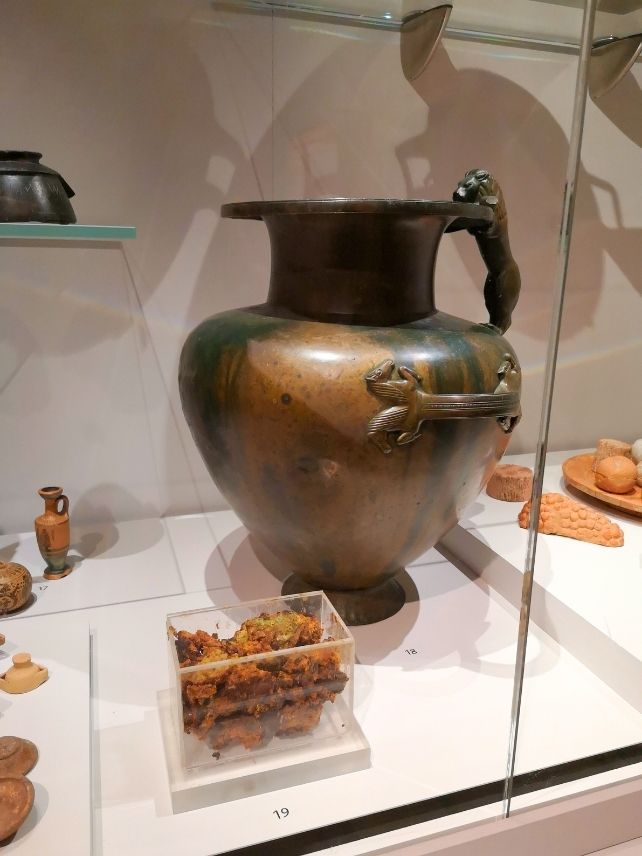 Bronze jar with orange gunk in clear plastic container next to it