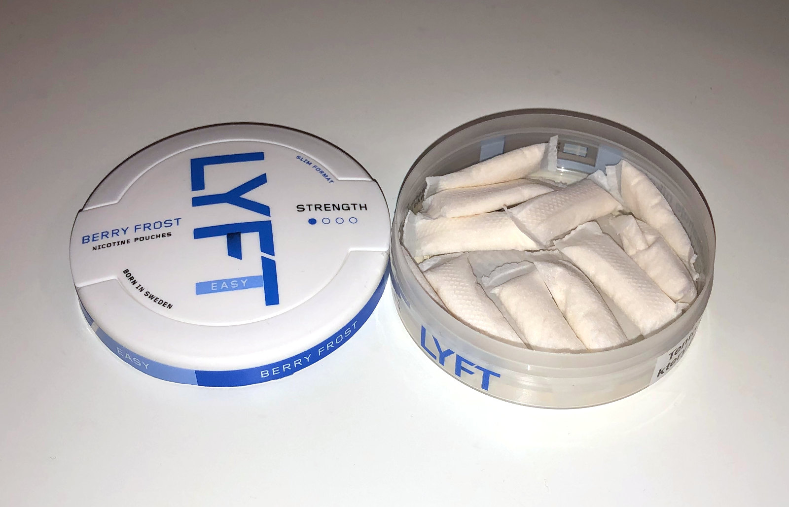 photo of a round, flat tin lying open on a white surface. inside the tin are several white pouches. the tin is labelled 'lyft' berry frost nicotine pouches, low strength