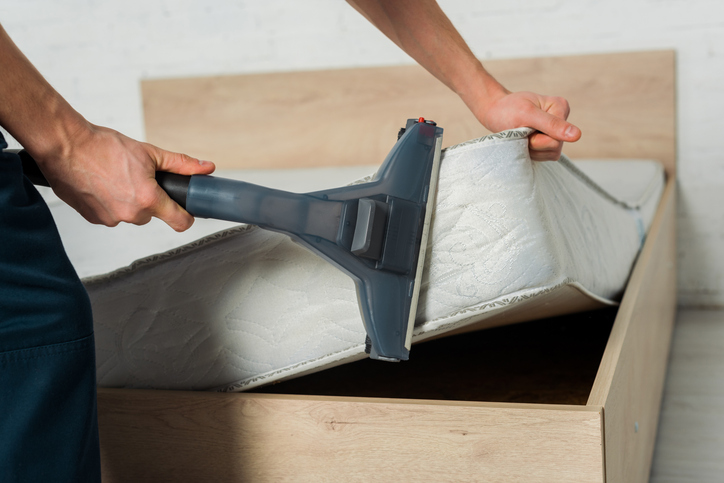 man lifting mattress to vacuum its sides