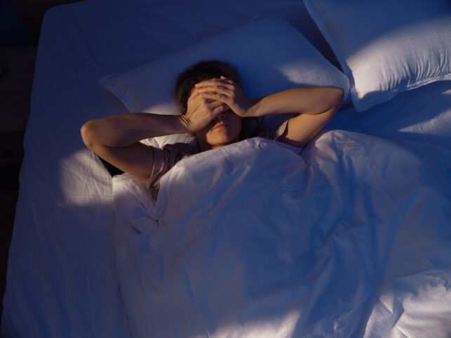 Woman covering eyes from light shining on dark bed