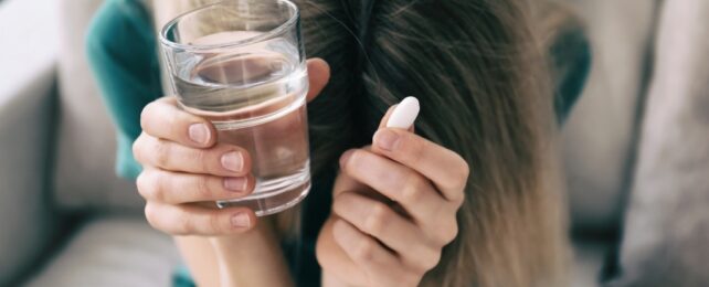 woman holding pill and a glass of water