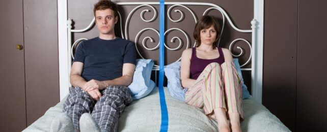 couple sitting in bed separated by a blue line