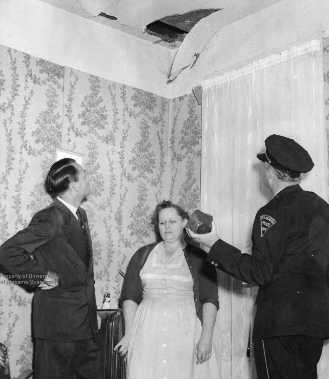 Two men, one holding meteorite and a woman standing under a hole in ceiling of a room