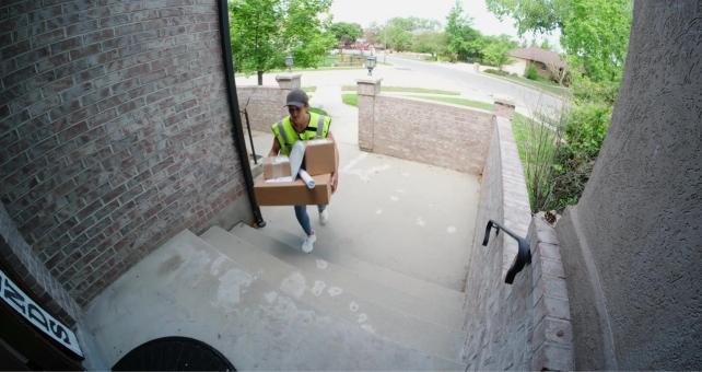a video monitor view of a person wearing a yellow safety vest carrying packages