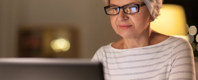 Happy senior woman in glasses using laptop at home in the evening
