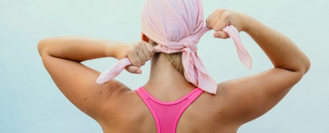 A woman facing away from viewer – wearing a racer-back top, tying a pink scarf across blond hair