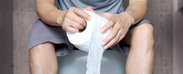 A person sitting on a toilet holding a toilet roll