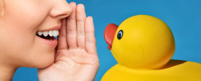 Person's mouth talking past a hand to a rubber duck