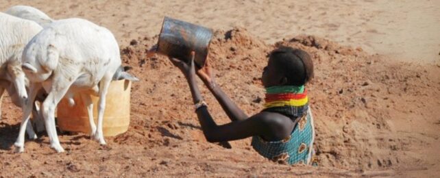 Woman in a hole in the barren ground with a tin of water