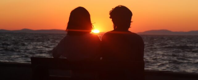 Silhouette of a Couple Sitting on Bench in Front of the Sea during Sunset