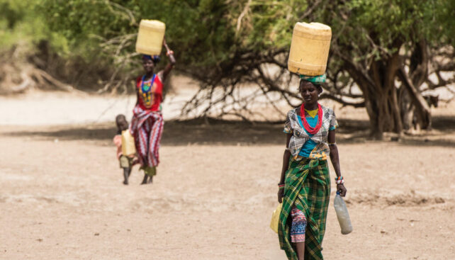 Two Turkana women carrying water through barren landscape