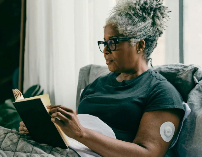 Woman with Diabetes Wearing a CGM Device on Her Arm Reading a Book
