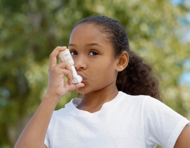 A girl aged around 8 using an inhaler outdoors