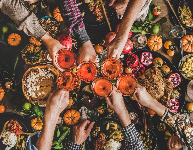 Aerial view of food and multiple hands holding glasses of wine in the center of image