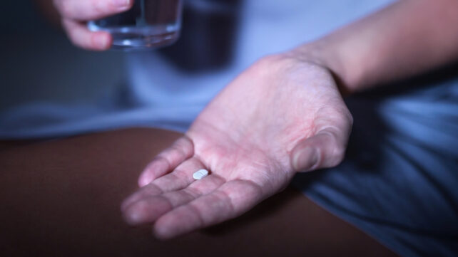 One pill in the hand of a person sitting on a bed