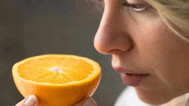 A woman holding a cut orange up to her nose