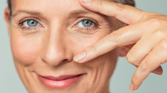 A smiling middle-aged woman is peeking through her open fingers