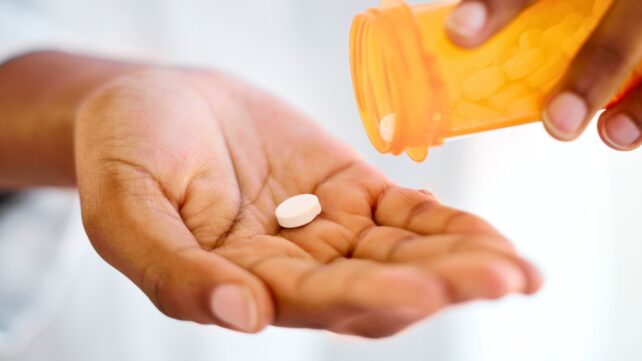 Generic white tablet spilled into a hand from a prescription bottle